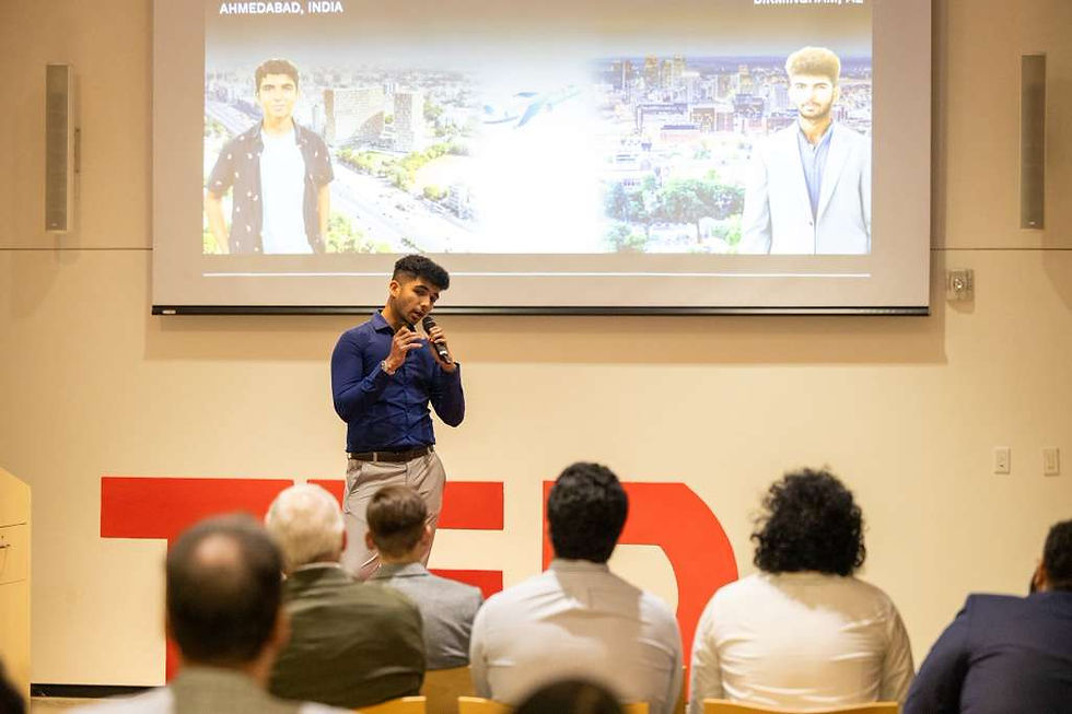 Man giving a presentation in front of a TEDx audience. Slide shows two city images: Ahmedabad, India, and Birmingham, UK. Audience is seated.