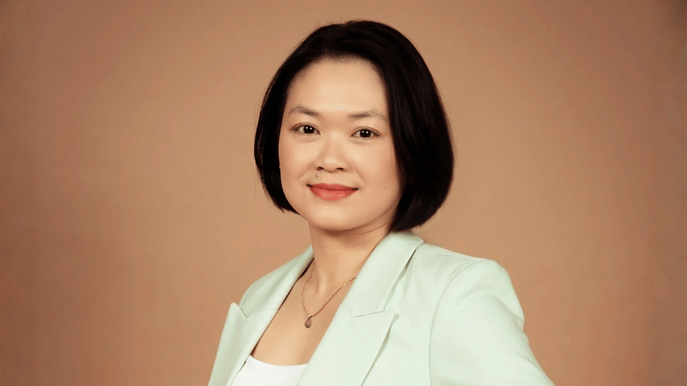 Portrait of a woman with a bob haircut in a mint blazer, smiling against a plain beige studio background.