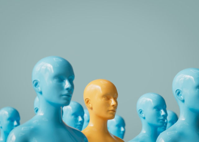 A group of glossy blue mannequins surrounds a single yellow mannequin, symbolizing individuality and standing out from the crowd.