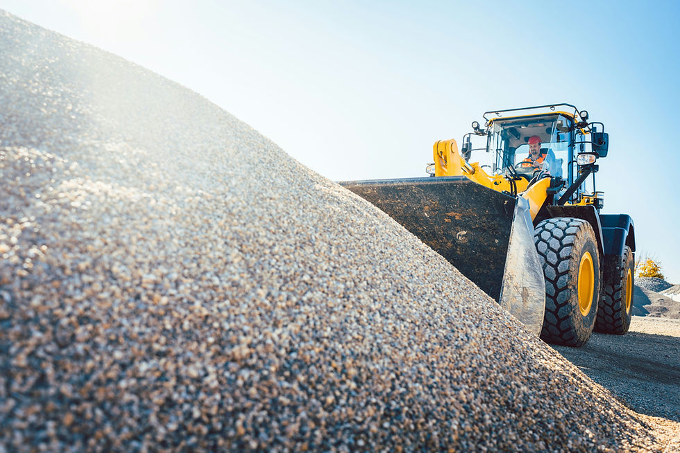 Yellow front loader with a driver moves gravel at a quarry under a bright blue sky, with a large gravel pile in the foreground.