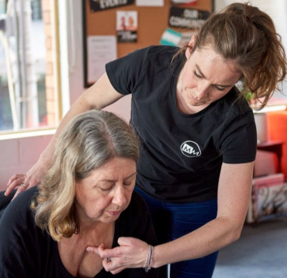 a woman providing physical therapy or bodywork to an older woman, guiding her posture and movement with care in a professional setting.