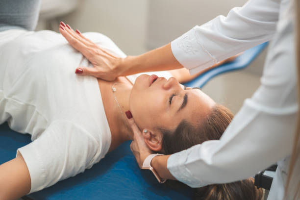 Woman receiving a neck massage on a blue table. Therapist's hand on her chest and neck. Relaxed expression, soft lighting.