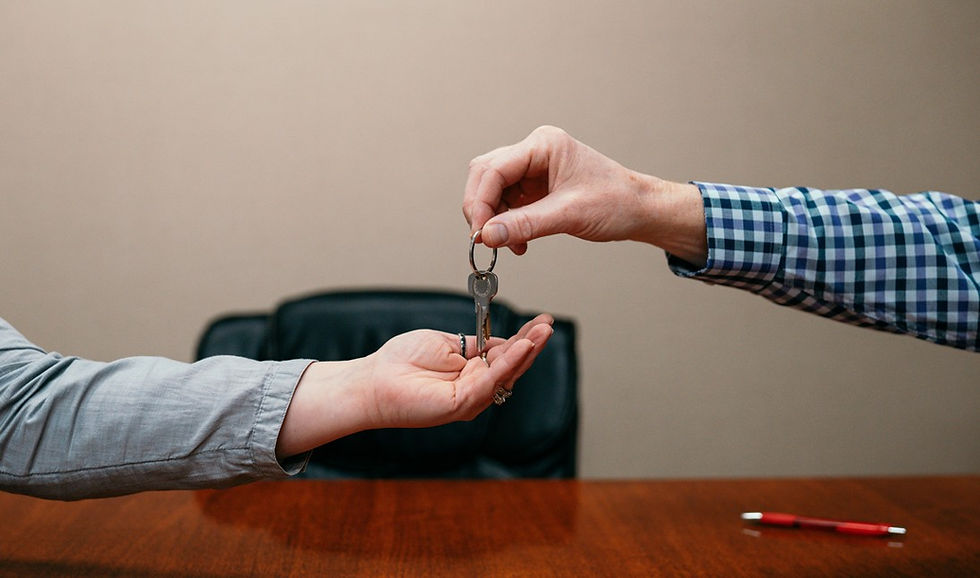 Two people exchange a key over a wooden table in an office, suggesting a handoff or property transfer.