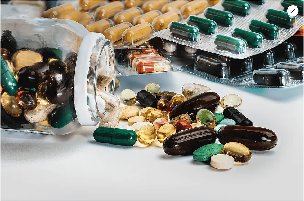 Spilled jar of multicolored capsules and pills on a white surface. Blister packs in the background. Vibrant, scattered arrangement.