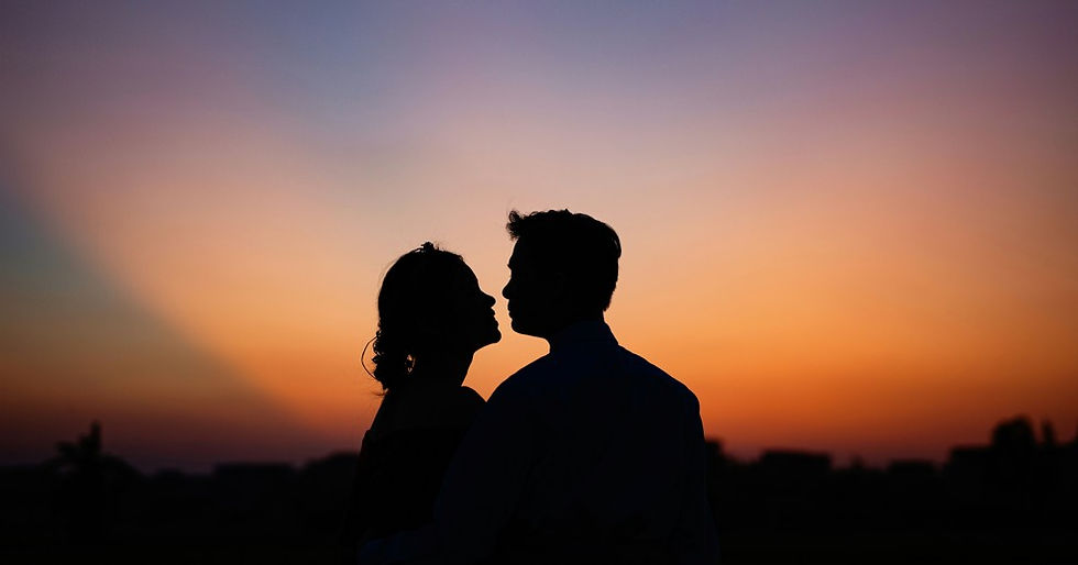 Silhouetted couple facing each other at sunset, with a warm orange and purple sky over a dark horizon.