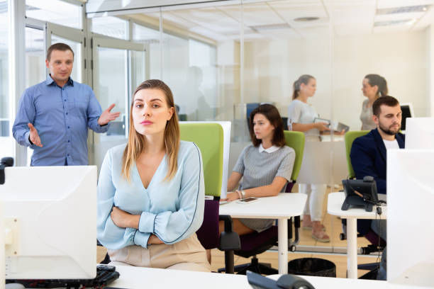 Upset unhappy girl sitting at laptop in coworking space while annoyed businessman pointing out mistakes in her work.
