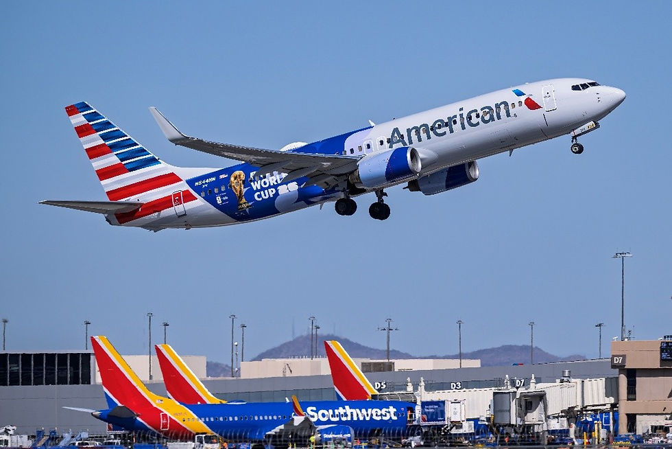 American Airlines World Cup-liveried jet takes off over airport, with Southwest planes and gates below under clear blue sky.