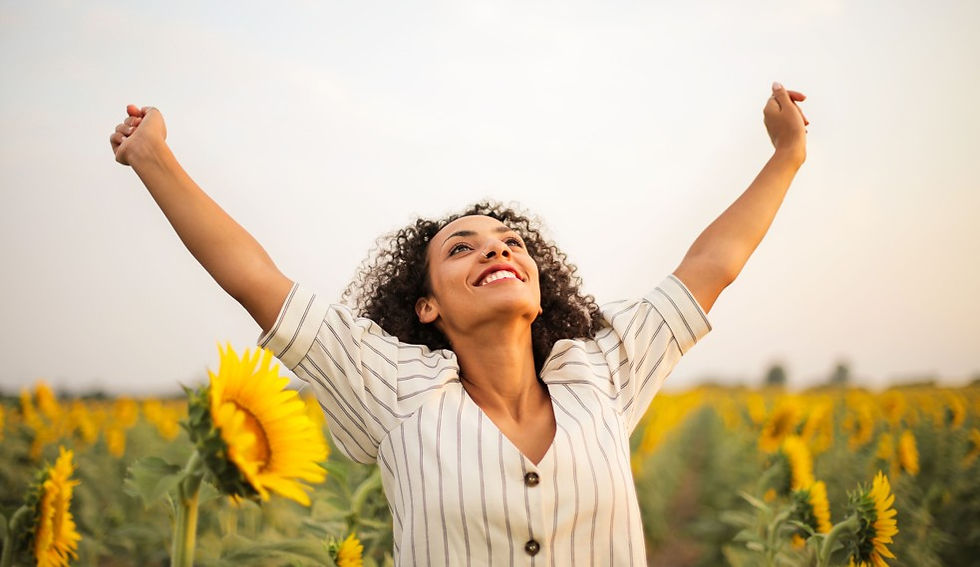 Smiling woman with arms raised in a sunflower field under a bright sky