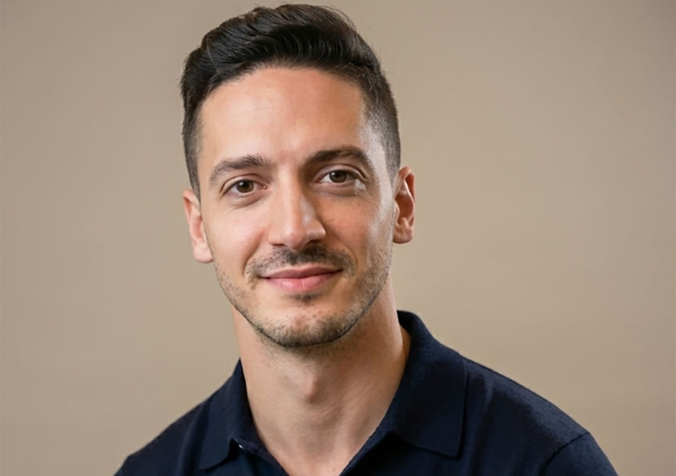 Smiling man with short dark hair wearing a navy shirt against a plain beige background. Calm and friendly expression.