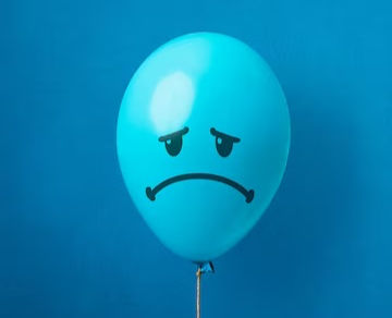 Blue balloon with a sad face drawn in black on a matching blue background. The mood is somber and reflective.