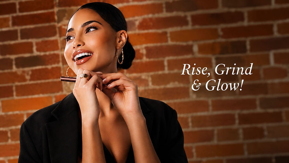 Smiling woman in black blazer applies makeup pencil before a brick wall; text reads Rise, Grind & Glow!