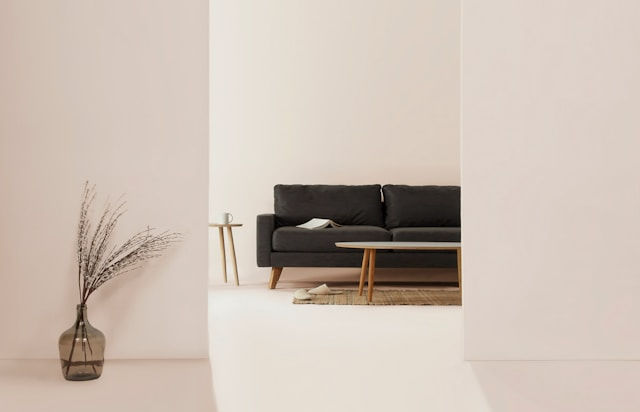 A minimalist living room features a dark sofa, a low wooden coffee table, and neutral-toned decor, viewed through a wide doorway.