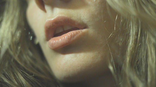 Close-up of a person's lips, lightly parted, with long, wavy hair framing the face. Warm lighting creates a soft, intimate mood.