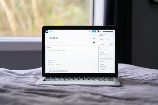 a laptop placed on a bed. The laptop screen displays a text editor or a content management system interface, possibly used for blogging or website design, 