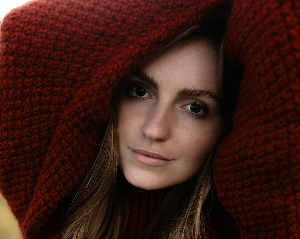 Woman with a calm expression wrapped in a textured red sweater, close-up. Brown hair frames her face. Cozy and intimate mood.