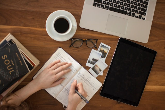 a women writing on a notebook in front of laptop