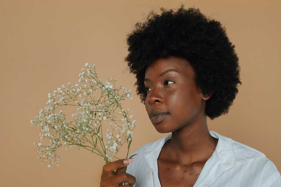 Woman with curly hair holds white flowers against a beige background, wearing a white shirt. Calm expression.