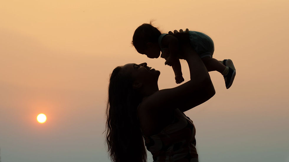 The photo shows a silhouette of a mother joyfully lifting her baby against the backdrop of a serene sunset.