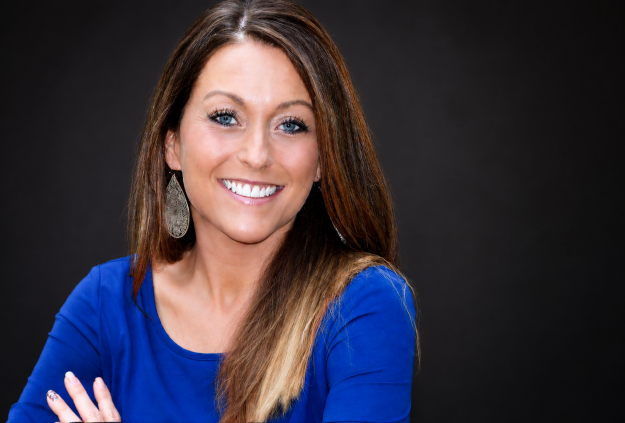 Smiling woman with long brown hair in a blue top against a dark background