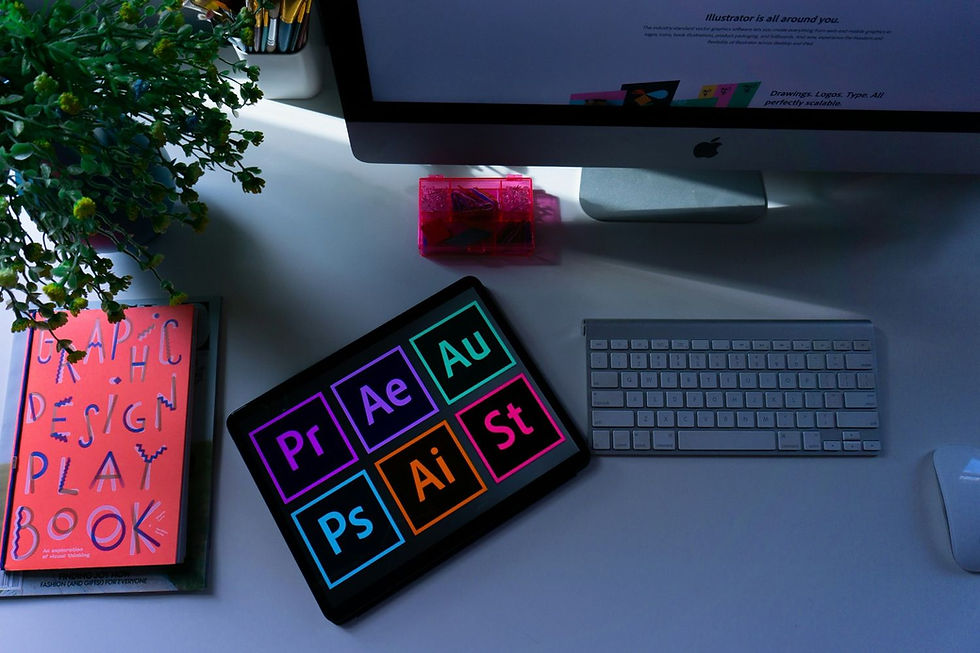 Tablet with colorful app icons, orange "Graphic Design Playbook," keyboard, mouse, and monitor on a white desk, alongside a plant.