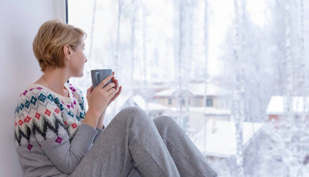 A woman sitting on the windowsill with a cup of tea 