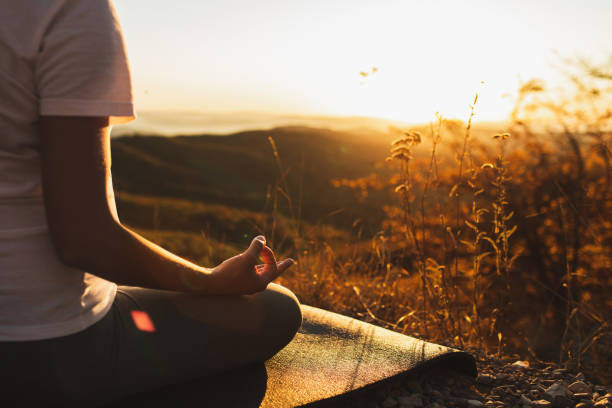 Person meditating on a mat at sunset in a grassy hill setting. Warm, golden tones dominate, creating a peaceful and serene mood.