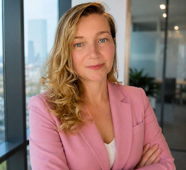 Portrait of a woman in a pink blazer, arms crossed, smiling softly in a bright modern office with city windows.