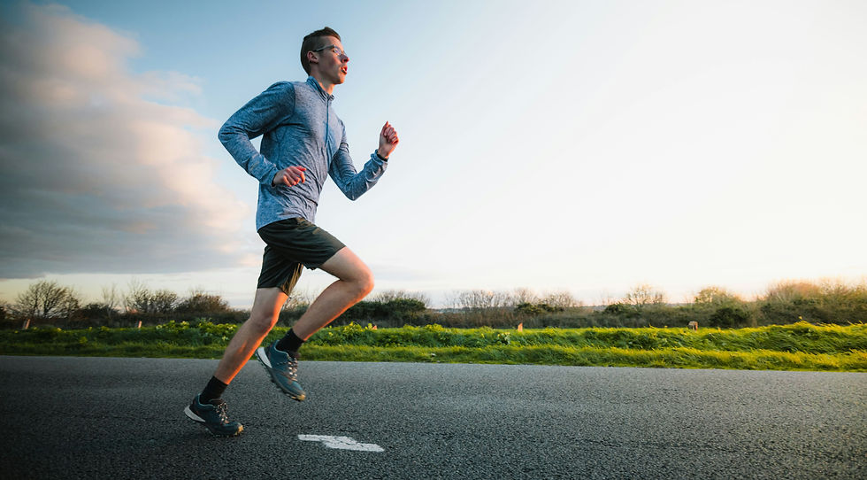 Male runner in glasses and gray top jogs along a country road at sunset under a cloudy sky.