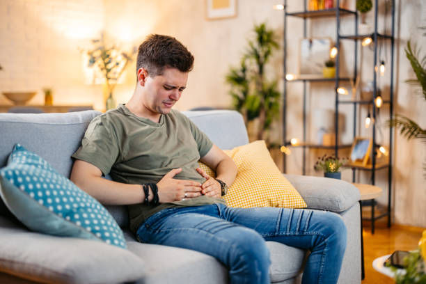 Young man having stomach pain while sitting on the sofa at home