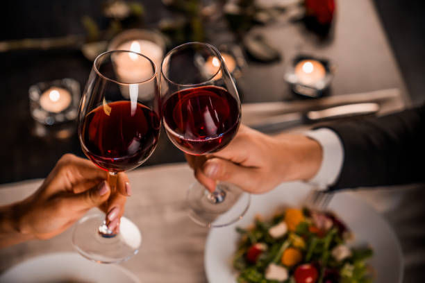 Hands clinking wine glasses over a candlelit table with salads. Romantic atmosphere, warm lighting, and elegant setting.