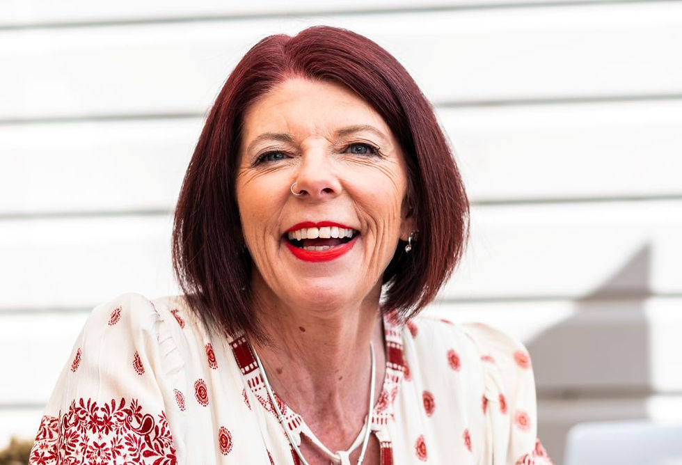 Woman with red hair smiles widely wearing a patterned white and red blouse. Background: light horizontal lines, bright and cheerful mood.