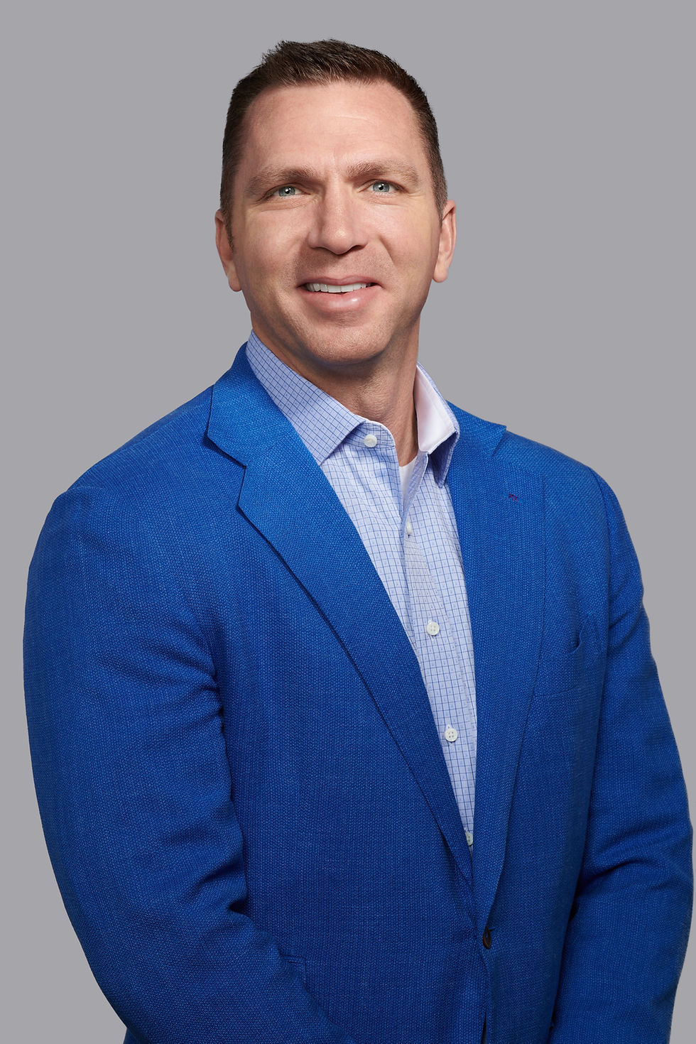 Smiling man in a bright blue blazer and checkered shirt posed against a plain gray studio background.