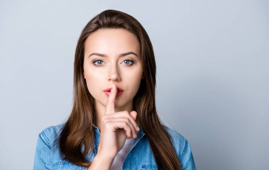 Close up portrait of young woman holding her forefinger on lips showing hush silence sign,