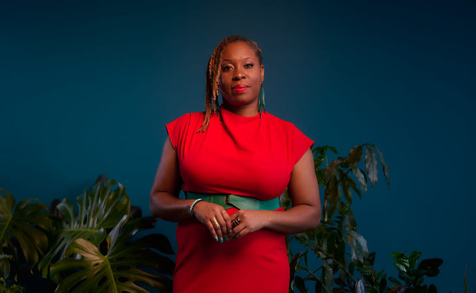 Woman in a red dress stands confidently against a blue background. Green plants surround her, adding a natural touch.