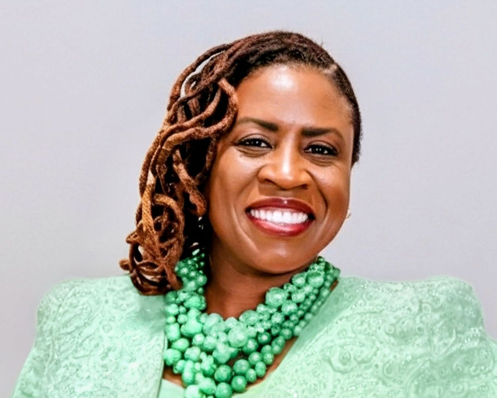Smiling woman in mint green lace and layered bead necklace, with braided hair, posed against a plain gray background.