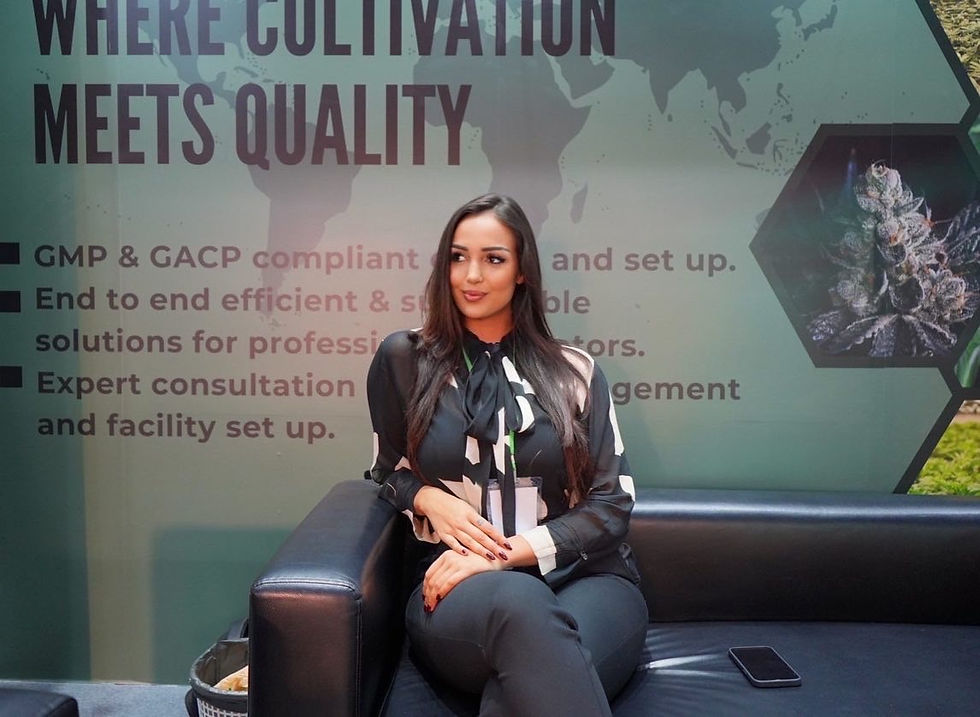 Woman in black blouse sits on a black couch at a trade show booth, with signage reading Where Cultivation Meets Quality.