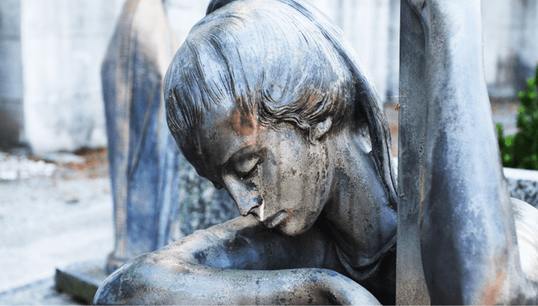 The image features a sorrowful stone statue of a grieving figure with a bowed head and closed eyes. The weathered texture and somber expression convey deep emotion, symbolizing loss, mourning, and remembrance. 