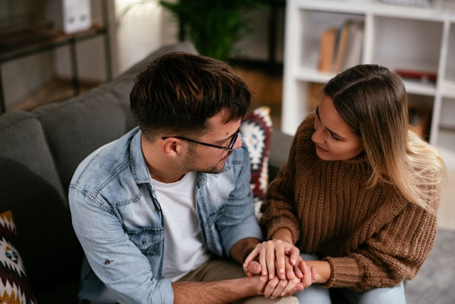 Young sitting on couch, girlfriend forgive boyfriend