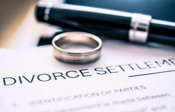 Ring and pen on a "Divorce Settlement" document, conveying formality and finality with a blue-toned background.