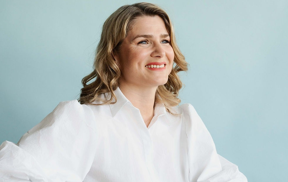Smiling blonde woman in a white blouse against a pale blue background, looking off to the side.