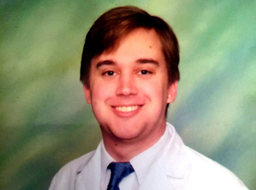 Smiling young man in white shirt and blue tie, posed in a school-style portrait against a mottled green backdrop.