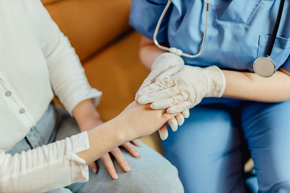 Nurse in blue scrubs and gloves gently holds a patient's hand in a warm clinic setting.
