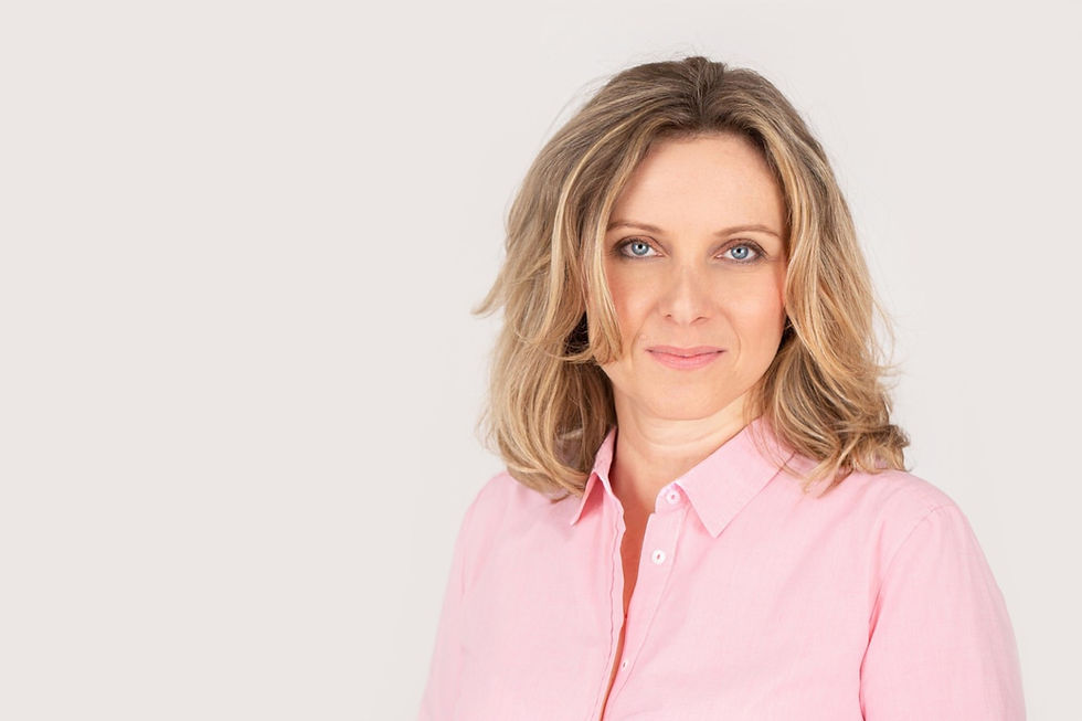 Woman with wavy blond hair in a pink shirt smiles subtly against a light gray background, giving a calm and confident vibe.