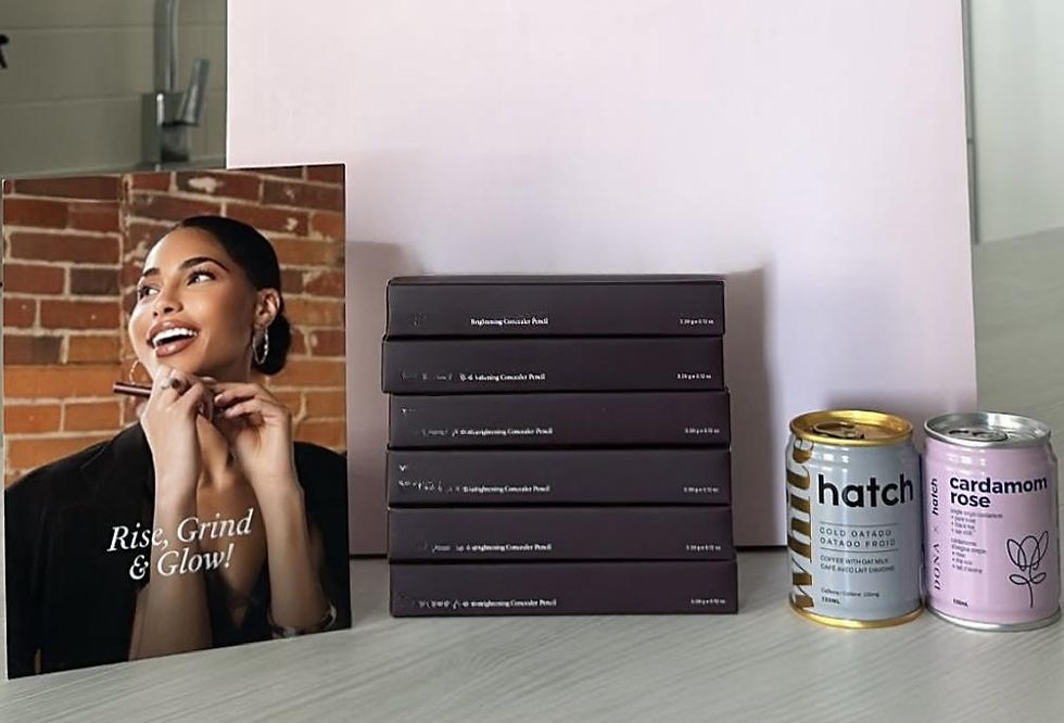 Beauty ad card reading Rise, Grind & Glow! beside stacked dark boxes and two drink cans on a table against a white backdrop.