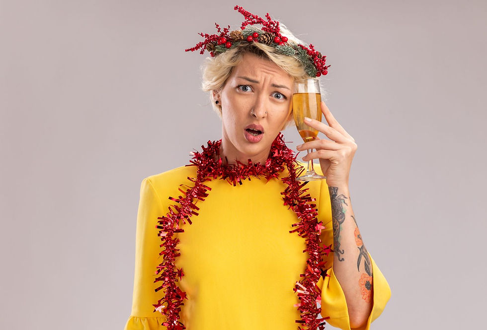 Woman in yellow dress with a red garland and a festive headpiece holds a champagne glass, looking surprised. Gray background.