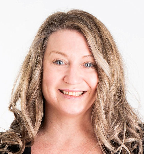 Smiling woman with long, wavy blonde hair against a white background, exudes happiness and warmth.