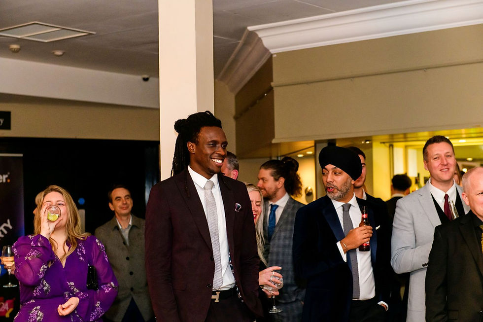 Guests in formal wear mingle at an indoor reception, smiling and sipping drinks under warm lighting.