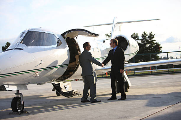 Two businessmen shake hands beside a private jet on a sunny airport tarmac.