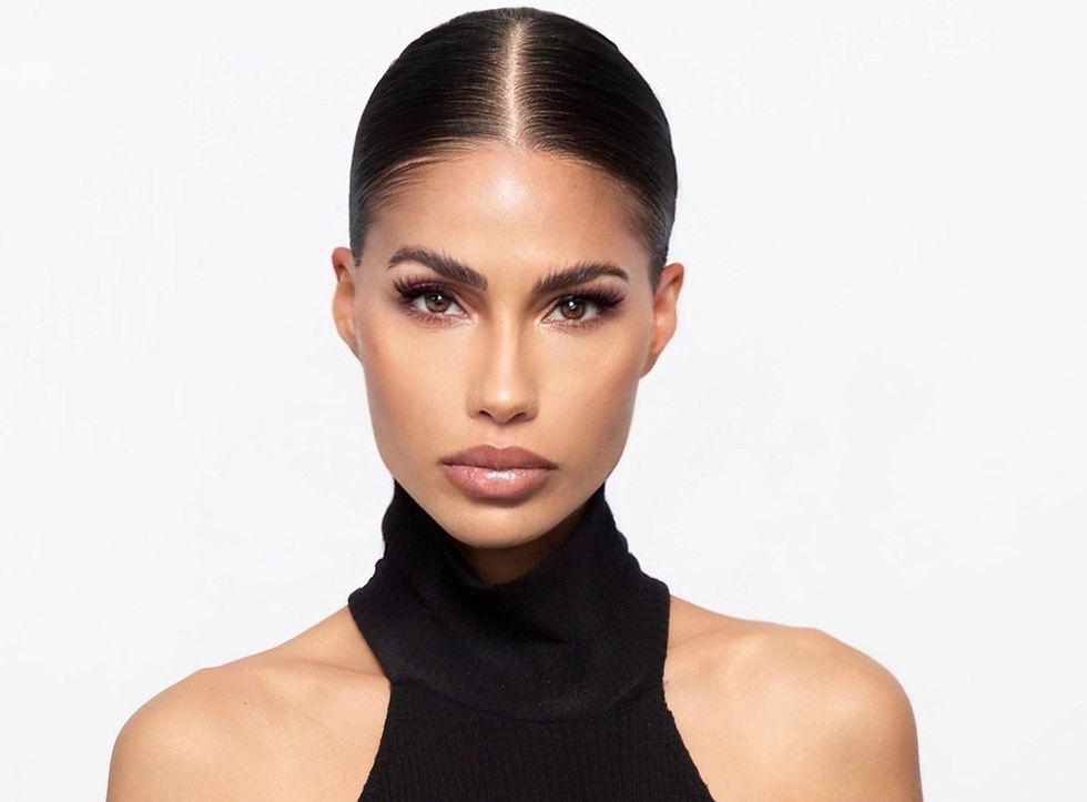 Studio portrait of a woman with sleek dark hair in a black halter top, staring calmly against a white background.