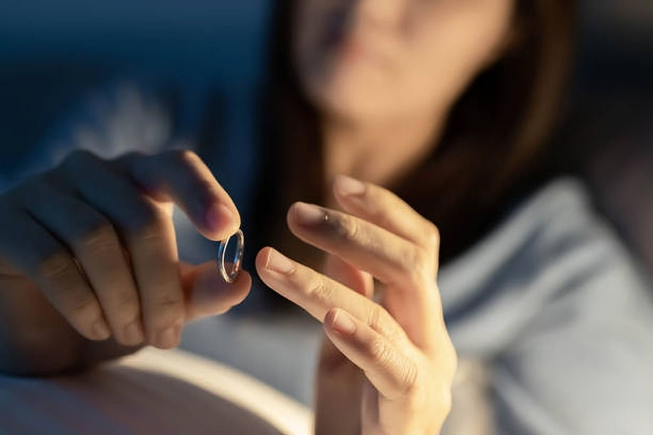 A person in soft lighting holds a silver ring, looking thoughtful. The background is blurred, suggesting an introspective or emotional mood.